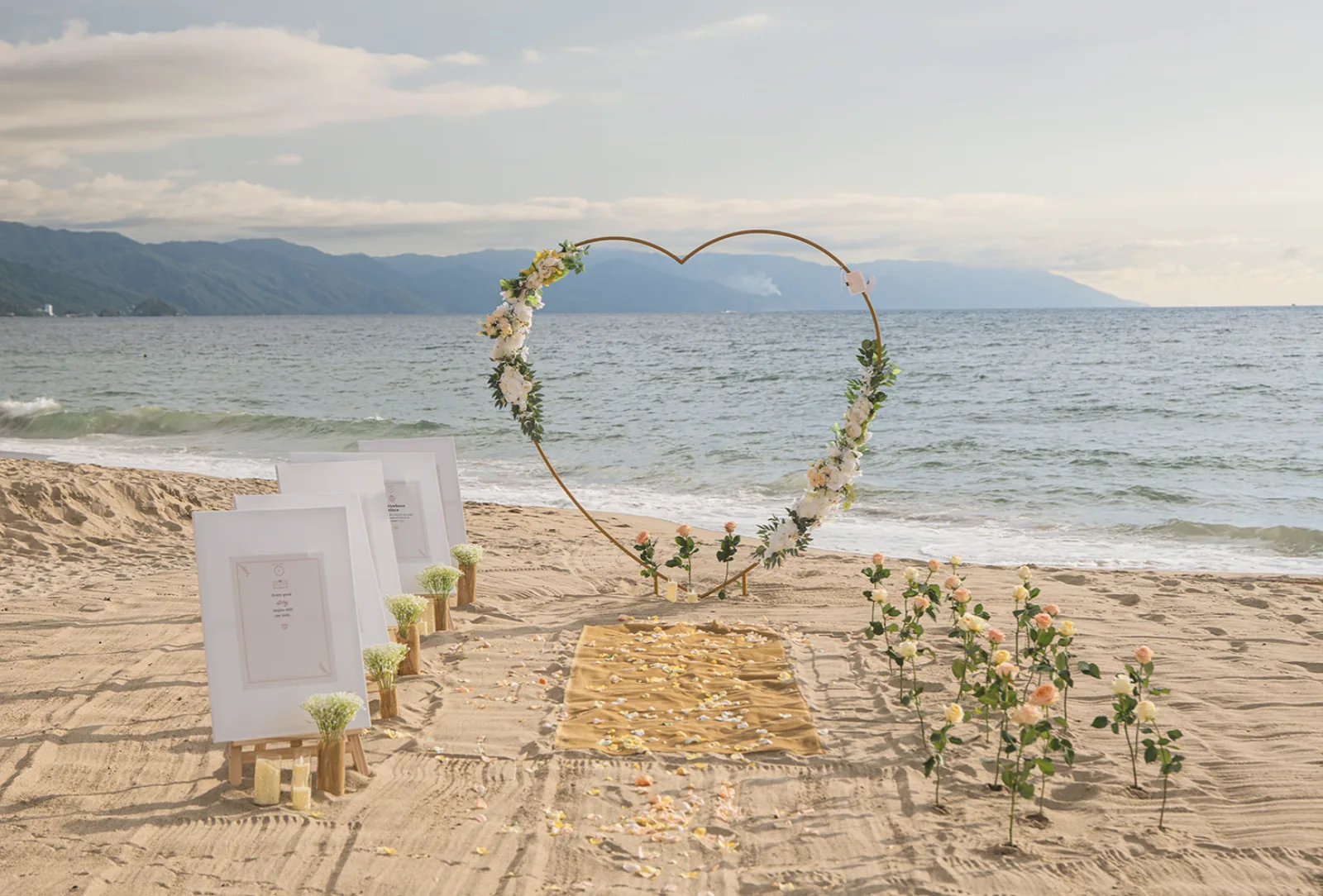 Beach proposal setup with floral heart arch and signage before the couple arrives